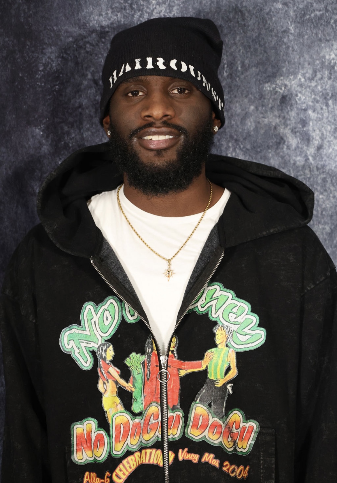 Model wearing a black Hairoun Studios knit cap, graphic hooded jacket, and star pendant